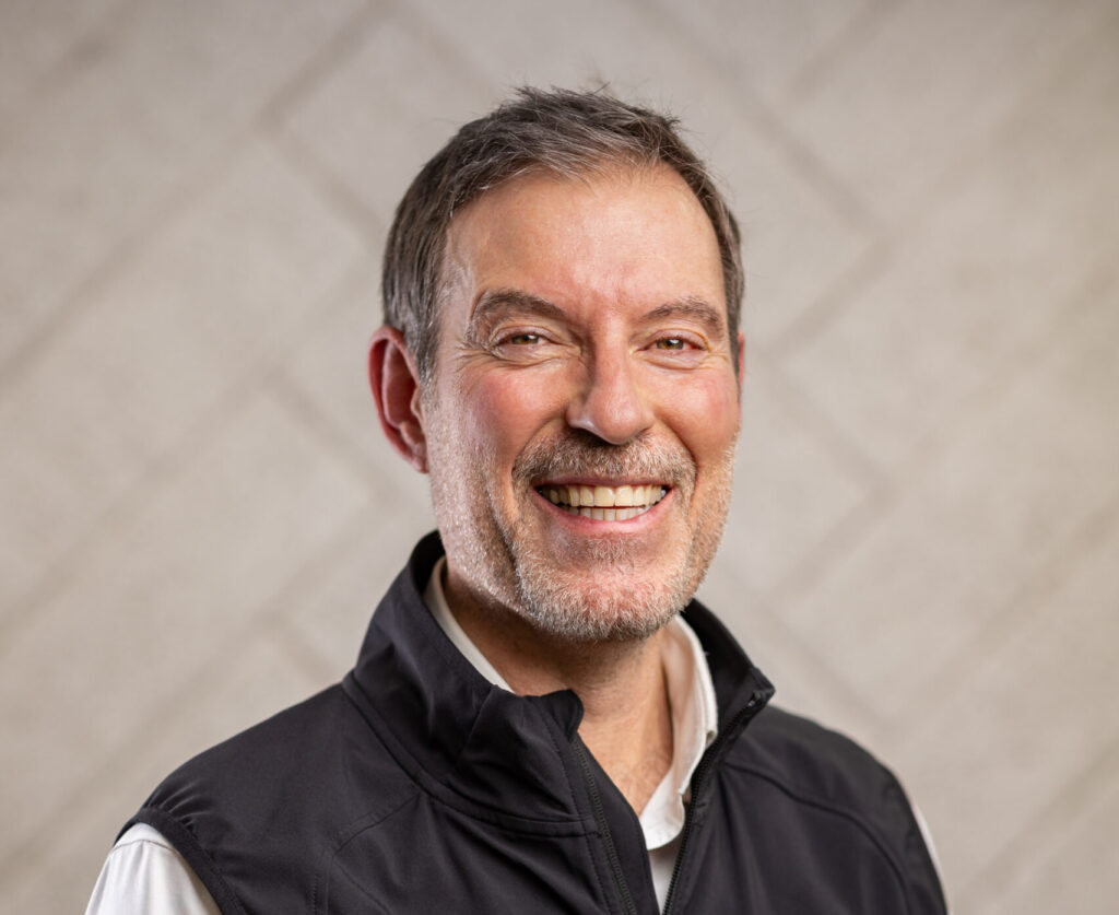 Smiling middle-aged man with short hair and light beard wearing a black vest