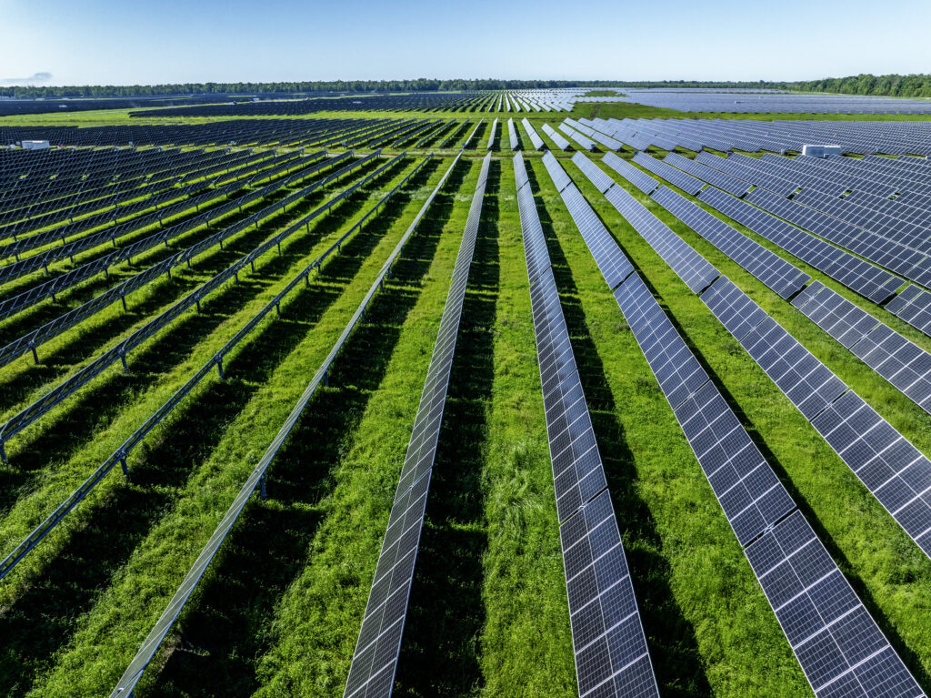 Aerial view of Oxbow Solar farm with rows of solar panels on green farmland.